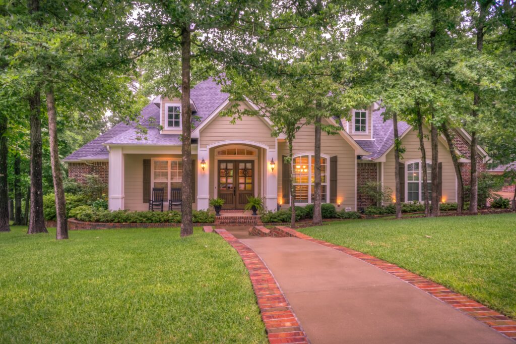 Charming Suburban Family Home For Sale With Brick Walkway, Manicured Lawn, And Tree-Lined Front Yard