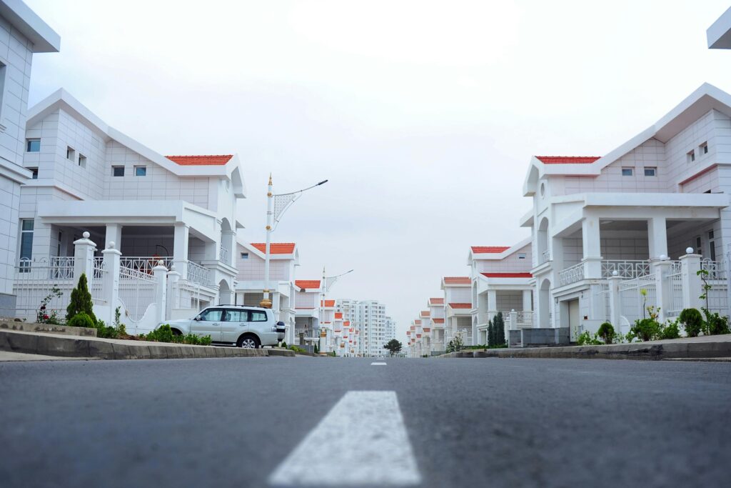 Modern White Residential Houses With Red Tile Roofs In Planned Community Development With Paved Roads And Landscaping.